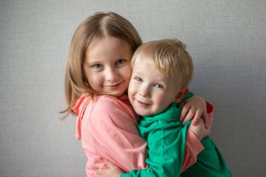 Mutlu ve gülümseyen iki çocuğun yakın plan portresi. Sarışın erkek ve kız kardeş kucaklaşması, kardeş ilişkisi kavramı. Komik çocuklar. Kız ve erkek sarılıyor..