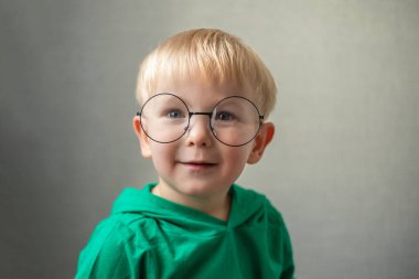 Yuvarlak gözlüklü küçük bir çocuğun portresi. Çocuk kameraya bakıp gülümsüyor..
