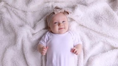 Beyaz bir battaniyenin üzerinde sırtüstü uzanmış kameraya bakan üç aylık tatlı bir bebeğin portresi. Çocukluk, yeni hayat, annelik kavramı..