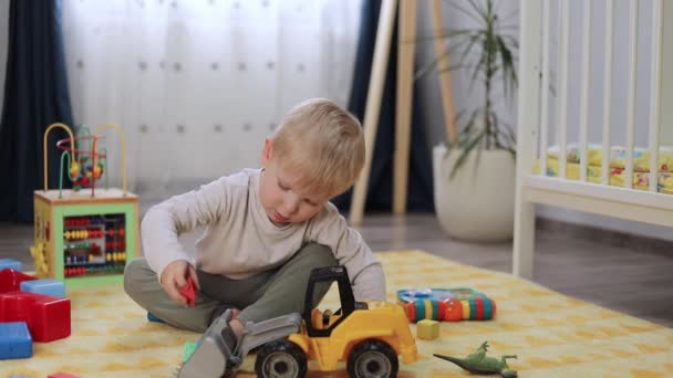 Счастливый ребенок играет с игрушечной машиной, сидя на полу в детской комнате — стоковое видео