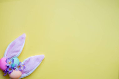 Tavşan kulakları, paskalya yumurtaları ve sarı arka planda bahar çiçekleri. Basit minimalizm düz görünüm kopyalama alanı.