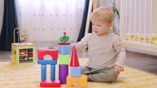 Милый маленький мальчик играет с блоками в детской комнате — стоковое видео