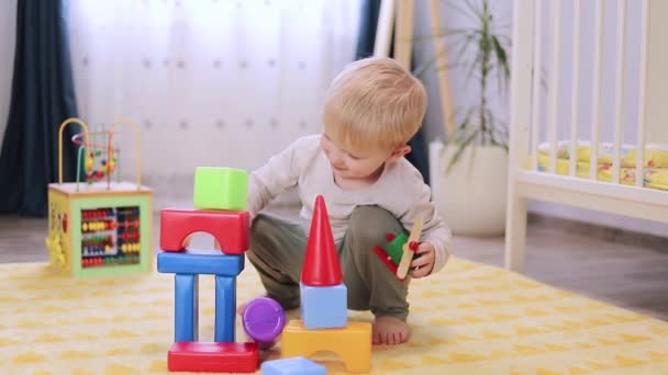 Милый маленький мальчик играет с блоками в детской комнате — стоковое видео