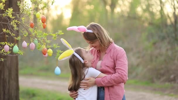 Ibu dan anak yang bahagia di telinga kelinci merayakan Paskah, memeluk, mencium dan menggosok hidung mereka dengan latar belakang matahari terbenam. Tradisi keluarga menghias pohon dengan telur Paskah — Stok Video