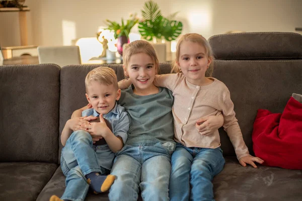 Porträt von drei Kindern zu Hause. Geschwister sitzen auf der Couch, umarmen sich und lächeln — Stockfoto