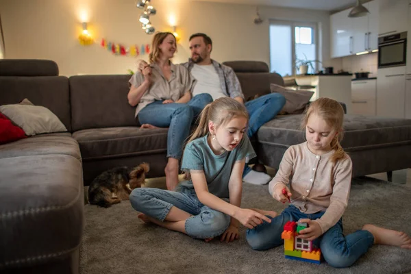 Kinderen, zussen veel plezier spelen op de vloer thuis terwijl ouders ontspannen op de bank — Stockfoto