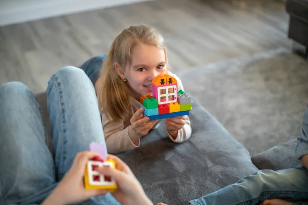 Kinderen spelen met blokken. De jongen zit op de bank en bouwt een huis van de bouwer — Stockfoto