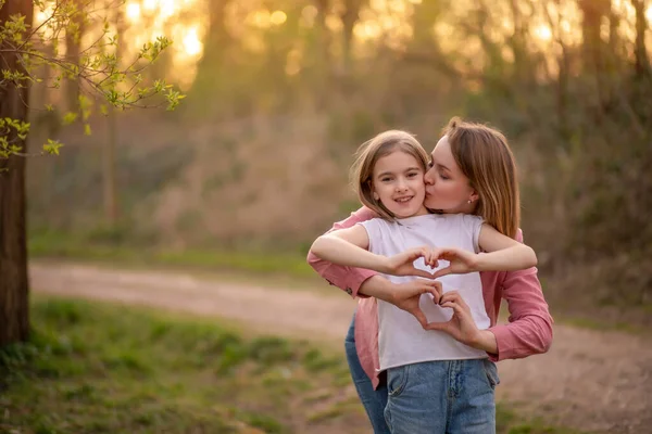 Mama i córka przytulają się i pokazują serce rękami. Dzień Matki — Zdjęcie stockowe