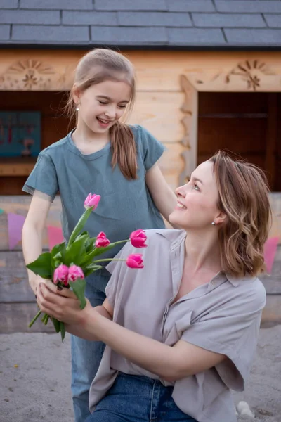 Gelukkige Moederdag. Kind dochter feliciteert moeder en geeft haar bloemen tulpen. Moeder en meisje glimlachen en knuffelen. — Stockfoto