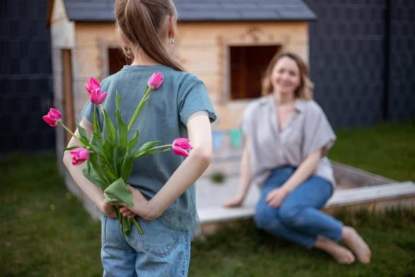 Gelukkige Moederdag. Kind dochter feliciteert moeder en geeft haar bloemen tulpen. Moeder en meisje glimlachen en knuffelen. — Stockfoto