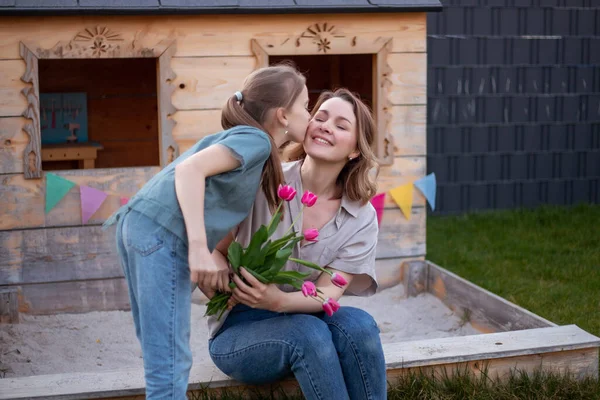 Szczęśliwego Dnia Matki. Córka gratuluje mamie i daje jej kwiaty tulipany. Mama i dziewczyna uśmiecha się i przytula. — Zdjęcie stockowe