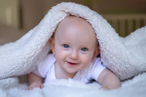 在白色毛毯下看着相机微笑的婴儿 — 图库照片