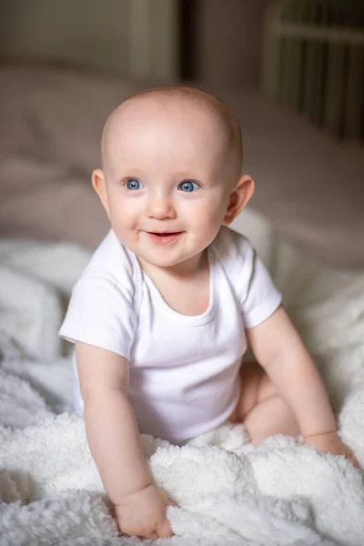 little cute baby sits on the bed on a white blanket.