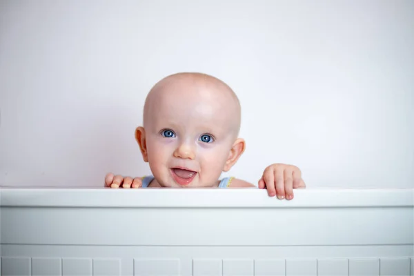 A small child peeks out on a white background. The child looks out of bed. peek-a-boo.