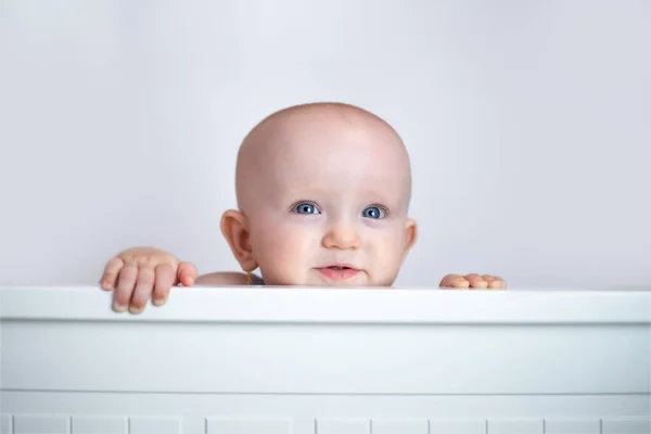 A small child peeks out on a white background. The child looks out of bed. peek-a-boo.