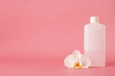 white plastic bottle for hand sanitizer with orchid flower isolated on pink background.