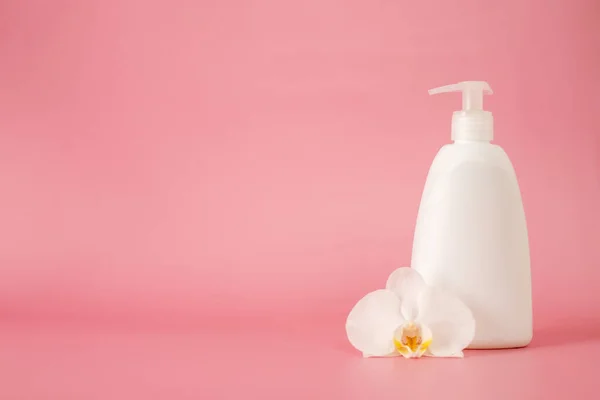 white cosmetic plastic bottle with pump dispenser pump and with orchid flower on pink background. Liquid container for gel, lotion, cream, shampoo, bath foam.
