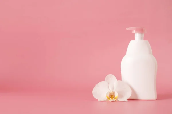 white cosmetic plastic bottle with pump dispenser pump and with orchid flower on pink background. Liquid container for gel, lotion, cream, shampoo, bath foam.
