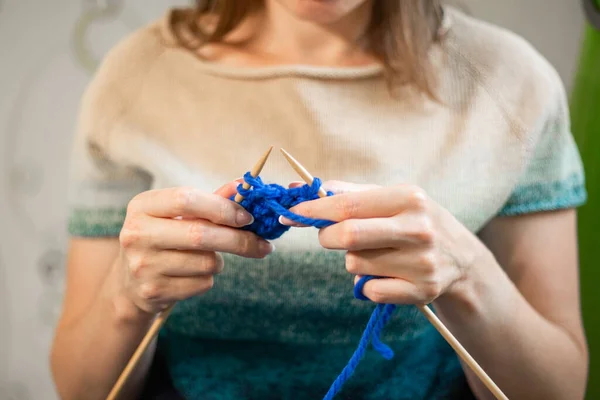 woman knitting a sweater from blue yarn.