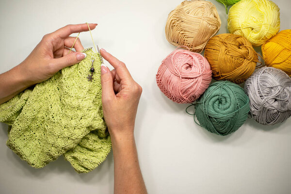 female hands knit a pullover, scarf or shawl with knitting needles from green yarn.
