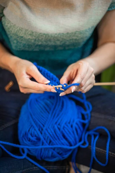 woman knitting a sweater from blue yarn.