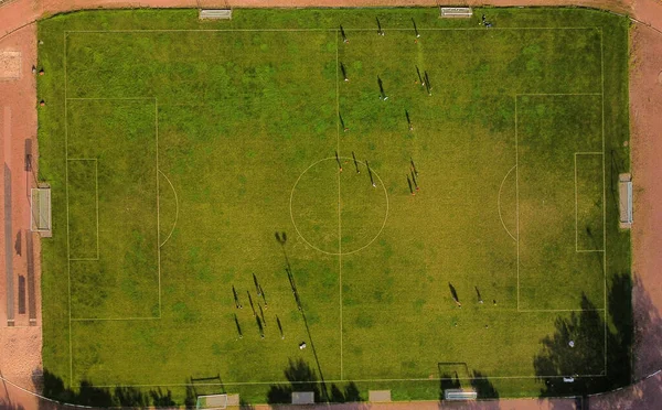 Aerial drone view from the sport center during the training of the football team. Players are playing a soccer match, aerial shot with a drone from a altitude at summer day.