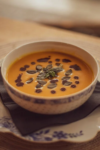 Pumpkin puree soup on a wooden background. Autumn cream soup decorated with pumpkin seeds and basil.