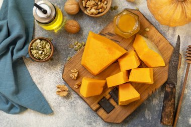 Raw pumpkin, honey, pumpkin seeds and nuts over gray stone background. Top view flat lay.