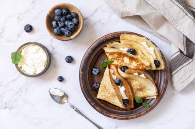 Krep gününü kutlamak, sağlıklı bir kahvaltı. Yaban mersinli ev yapımı leziz krepler ve taş bir masanın üstünde ricota. Üst görünüm düzlüğü. 
