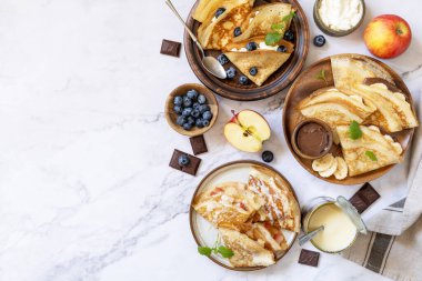 Krep gününü kutlamak, sağlıklı bir kahvaltı. Yaban mersinli ev yapımı krep, ricotta, elma, muz ve çikolata mermer bir masanın üstünde. En üstteki düz yerde. Boşluğu kopyala.