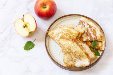 Krep gününü kutlamak, sağlıklı bir kahvaltı. Elmalı ev yapımı tatlı krepler ve mermer bir masanın üstünde konsantre süt..