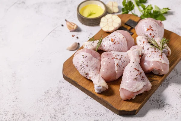 Chicken meat. Raw fresh chicken drumsticks with spices on a woden cutting board on a stone countertop. Copy space.