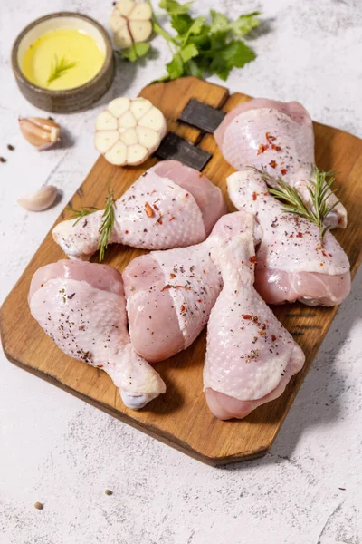Chicken meat. Raw fresh chicken drumsticks with spices on a woden cutting board on a stone countertop.
