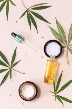 SPA organic beauty product. Herbal Alternative Medicine Concept. Cannabis cosmetic cream, face serum and hemp leaves over beige background. Top view flat lay.