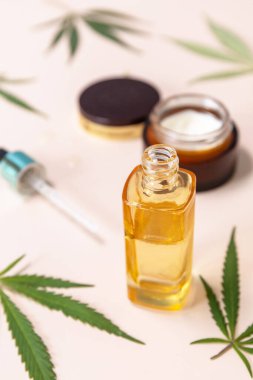 SPA organic beauty product. Herbal Alternative Medicine Concept. Cannabis cosmetic cream, face serum and hemp leaves over beige background. 