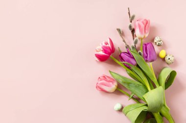 Paskalya kompozisyonu, renkli Paskalya yumurtaları ve bahar çiçekleriyle pembe arka planda laleler. Bahar ve Paskalya bayramı konsepti. En üstteki düz yerde. Boşluğu kopyala.