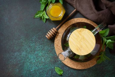 Therapeutic herbal green tea. Hot tea with honey mints in a glass teapot on a stone table. Top view flat lay. Copy space.