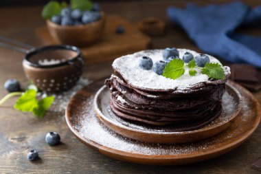 Pancake day, summer dessert. Delicious homemade american bananas chocolate pancakes with blueberries on a rustic table.