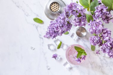 Lilac drink, infused drink from lilac flowers. Organic natural daikiri cocktail or mocktail, lilac lemonade with ice on a marble table. View from above. Copy space.