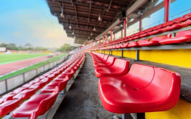 Taraftarlar için tribünde boş kırmızı koltuk akşam gökyüzüyle futbol stadyumunda tezahürat yapıyor.