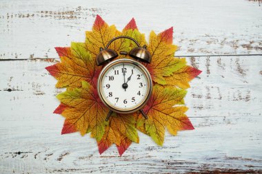 Ahşap zemin üzerinde akçaağaç yaprakları olan çalar saat