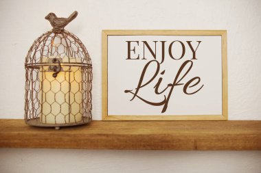 Üzerinde ENJOY Life yazan karatahta ahşap raflardaki sulama bitkilerindeki yapay bitkilerle dekore ediliyor.