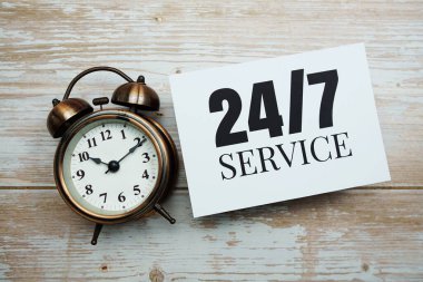 Ahşap arkaplanda 7 / 24 hizmet metni ve alarm saati