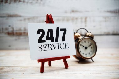 Ahşap arkaplanda 7 / 24 hizmet metni ve alarm saati