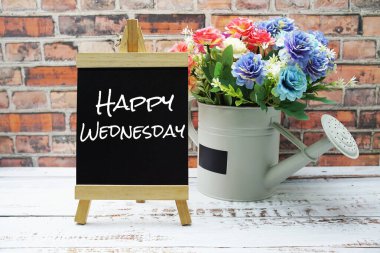 Kara ahşap sehpa ve vazo üzerine mutlu çarşamba metinleri. Duvarda çiçek buketi var.