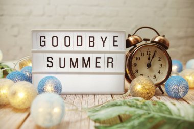 Güle güle. Çalar saat ve ahşap arka planda LED pamuk topları olan ışıklı kutuda yaz kelimesi.