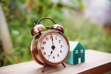 Çalar saat ve ev modeli yeşil arka planlı masada.