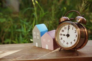 Çalar saat ve ev modeli yeşil arka planlı masada.