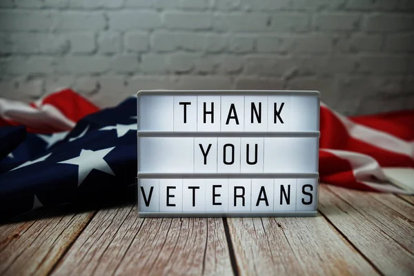 Thank You Veterans word in lightbox and American flag on wooden background