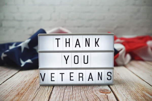 Thank You Veterans word in lightbox and American flag on wooden background